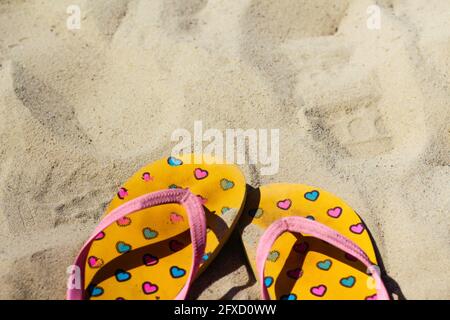 Defocus dirty bright yellow and pink slippers flip flops with pink and blue hearts on the sand. Summer background.The concept of heat, relaxation and Stock Photo