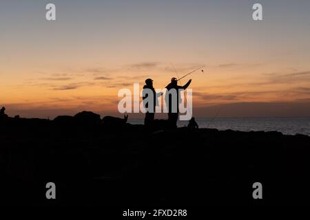 Silhouettes of two fishermen getting ready at sunset in front of the sea in Majorca. Fishing concept Stock Photo