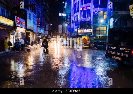 Nepali man cycling in Kathmandu main streets of Thamel during heavy monsoon rain at night time in Nepal. Stock Photo