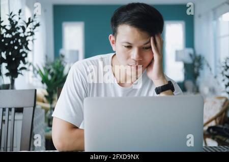 Thoughtful serious young man solving online problem doing resear Stock Photo