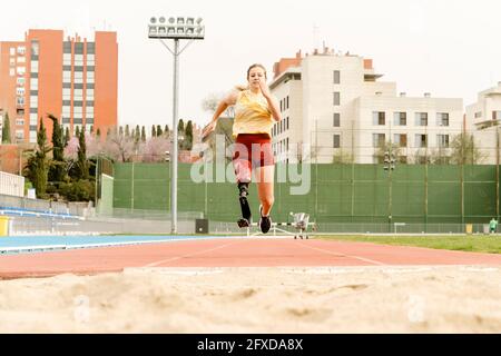 Female athlete with disability running towards sandpit Stock Photo