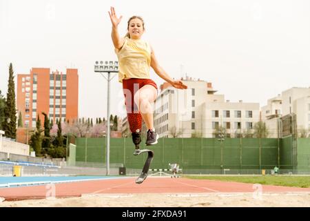 Female athlete with disability running towards sandpit Stock Photo