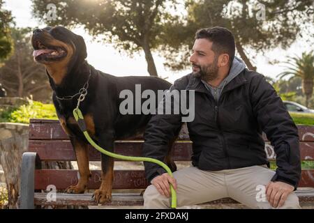 Man sitting on a park bench next to his rottweiler dog Stock Photo