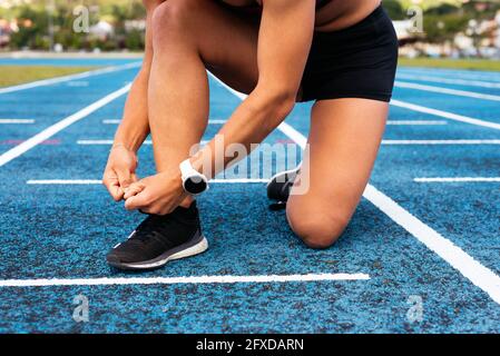 Crop young sportswoman tying shoelaces on track Stock Photo