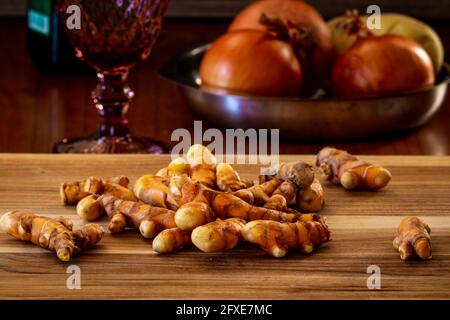 Raw fresh turmeric roots on a wooden table with onions and potatoe on the background. Stock Photo