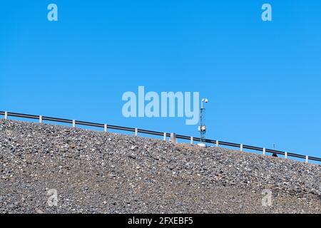 A surveillance camera by a guardrail on a highway sloping upward Stock Photo