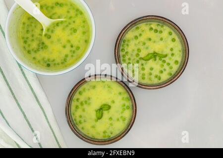 Creamy celery soup with green peas and fresh basilclose up in bowls on light grey marble background, view from above, copy space Stock Photo