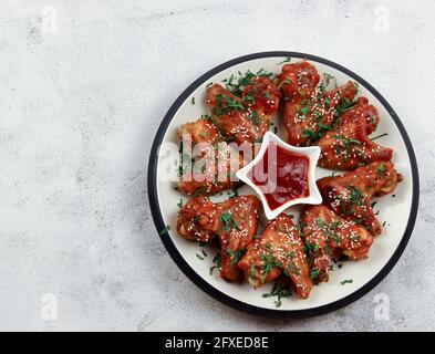 Spicy chicken wings with tomato sauce on a round plate on a light gray background. Top view, flat lay Stock Photo