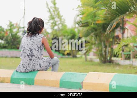 Back view of Sad Young Little sitting alone at park with copy space - Concept of loneliness, depression, unhappy and thoughtful Stock Photo