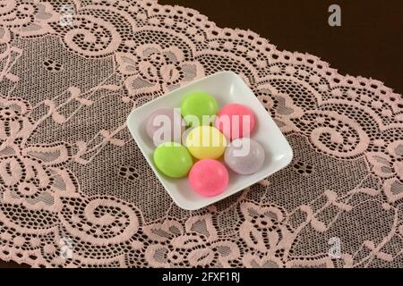 Multicolor soda pop mint candies small white candy dish on pink lace table runner on brown tablecloth Stock Photo