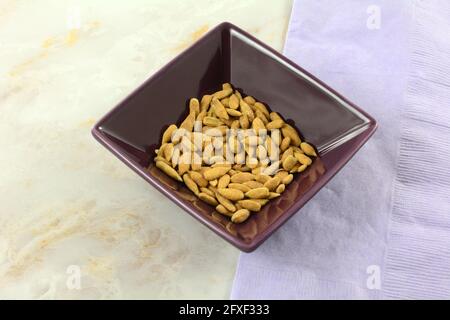 Roasted sunflower seeds with sweet corn and cheese flavoring in small purple snack bowl with lavender napkin Stock Photo