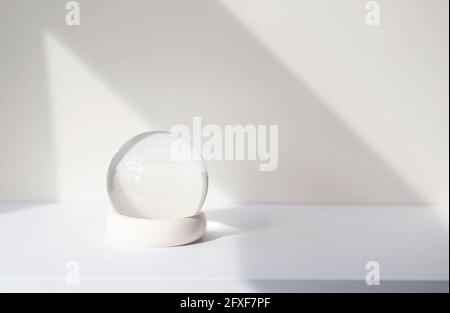 Minimal composition with glass ball on white desk, glass globe ball as decoration of interior. Abstract shadow lines on the wall, space for text, mock Stock Photo