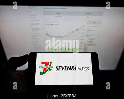 Person holding smartphone with logo of Japanese retail company Seven and i Holdings Co. Ltd. on screen in front of website. Focus on phone display. Stock Photo