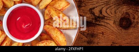 Ketchup and baked potato wedges close-up, a panoramic banner for a menu with a place for text, on a dark rustic wooden background Stock Photo