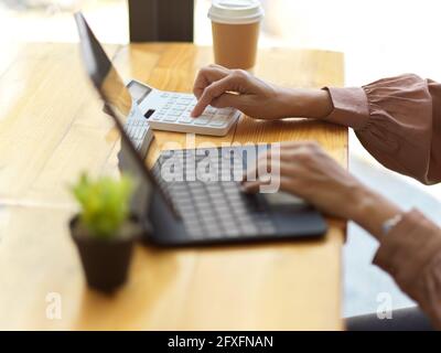 Side view of female office worker using digital tablet and calculator on wooden table in cafe Stock Photo