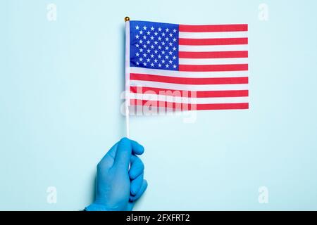 USA medicine and health care concept. A hand in a medical glove holds the US national flag on a light blue background. Day of the medical worker. High quality photo Stock Photo