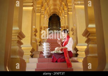 Myanmar women holding flowers at a temple. Southeast Asian young girls with burmese traditional dress visiting a Buddihist temple Stock Photo