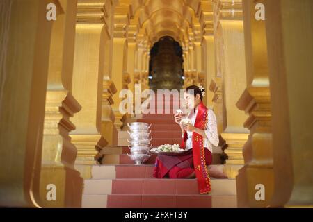 Myanmar women holding flowers at a temple. Southeast Asian young girls with burmese traditional dress visiting a Buddihist temple Stock Photo