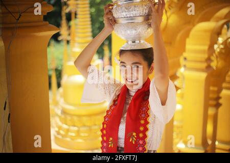 Young girl with traditional Burmese holding bowl of rice on the hand at beautiful golden pagoda in Myanmar Stock Photo