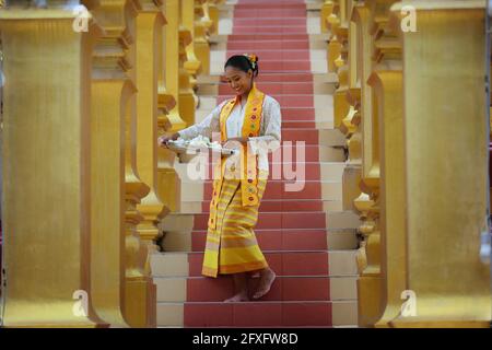 Myanmar women holding flowers at a temple. Southeast Asian young girls with burmese traditional dress visiting a Buddihist temple Stock Photo