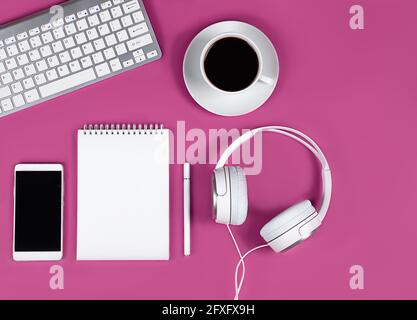 Keyboard, smartphone, headphones, notepad and pen on pink background, white cup of coffee. Concept - online training, education, remote operation, web Stock Photo