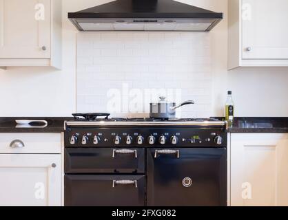 Black and white kitchen design. Painted wood modern kitchen with black enamel range cooker and chimney hood. UK shaker style kitchen remodeling Stock Photo
