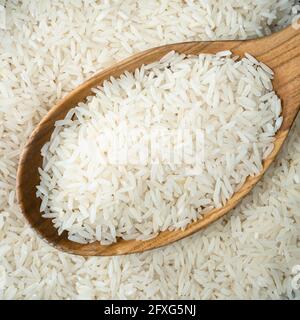 top view of raw long-grain polished rice in wooden spoon closeup