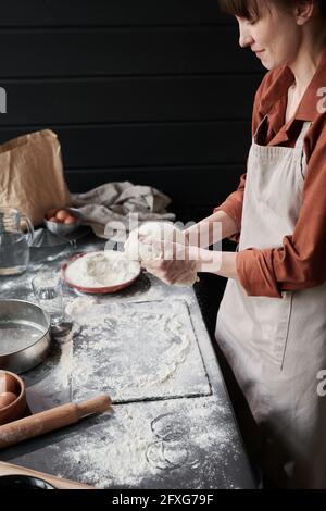 Young woman in apron making a dough to bake a cake in the kitchen Stock Photo