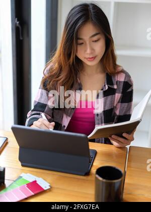 Top view of young female student looking no notebook and working digital tablet in library Stock Photo