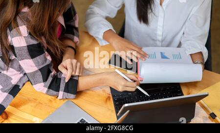 Top view of two female students doing group assignment together with digital tablet and documents on wooden table Stock Photo