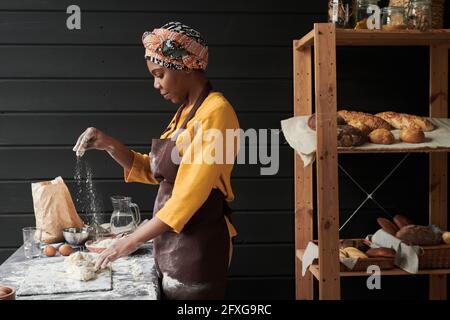 African baker in apron making a dough and baking homemade bread while working in the bakery Stock Photo