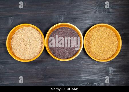 top view of white, black, yellow mustard seeds in ceramic bowls on black wooden table Stock Photo