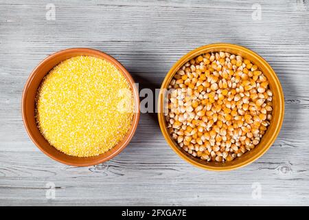 top view of corn seeds and cornmeal in round ceramic bowls on gray wooden table Stock Photo