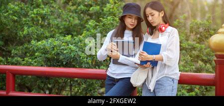Cropped shot of two young beautiful university students having conversation about textbook while standing at the park in university Stock Photo