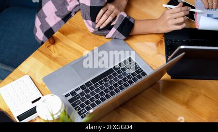 Top view of comfortable workspace with laptop, calculator and two people consulting on their work Stock Photo