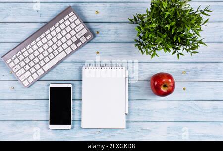 Cavitature and smartphone on a wooden desktop, on a blue background, notepad and handle, an apple for snack. Concept - online learning, remote job, we Stock Photo