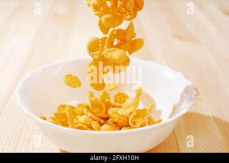 cereals falling in a white bowl on a wooden table Stock Photo