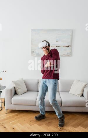 scared man in vr headset covering mouth with hand while gaming at home Stock Photo
