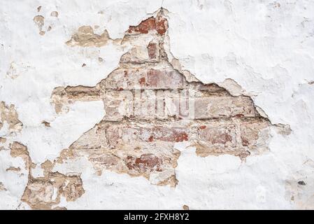 Wall of old building with large hole in chipped white stucco Stock Photo
