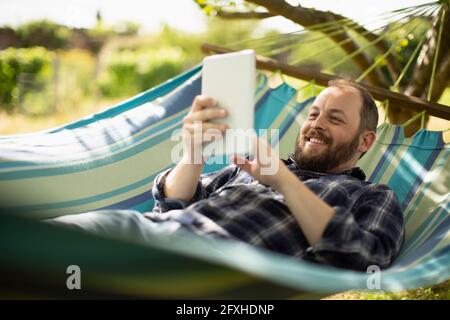 Happy man using digital tablet in sunny summer hammock Stock Photo