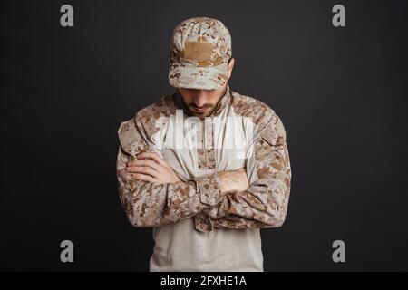 Close up of a handsome pensive young military man in uniform thinking isolated over black background Stock Photo