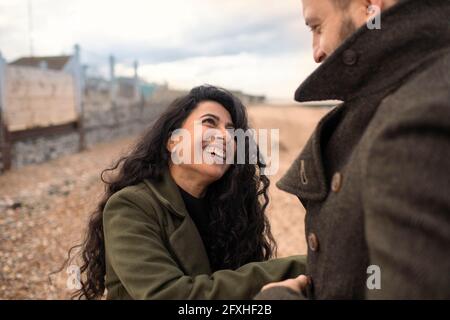 Happy playful couple in winter coats on beach Stock Photo