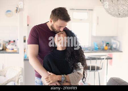 Happy affectionate couple hugging and kissing in kitchen Stock Photo