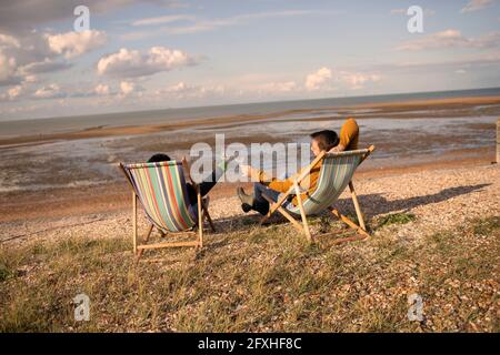 Couple toasting wine glasses from chairs on sunny winter beach Stock Photo