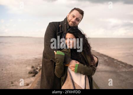 Portrait affectionate couple hugging on winter ocean jetty Stock Photo