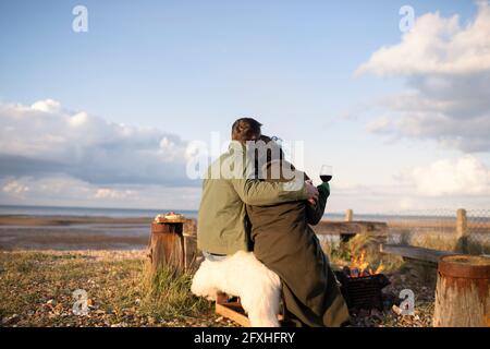 Affectionate couple hugging and drinking wine on sunny winter beach Stock Photo