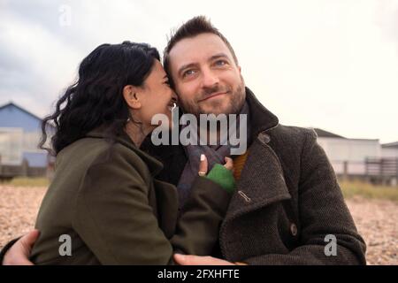 Happy affectionate couple in winter coats hugging on beach Stock Photo