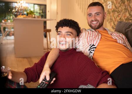 Happy gay male couple watching TV on sofa Stock Photo