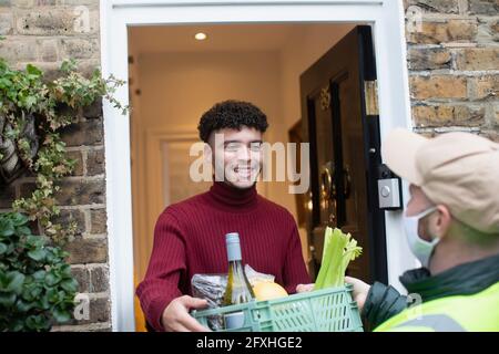 Happy man receiving grocery delivery from delivery man in face mask Stock Photo