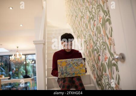 Young man using laptop on apartment stairs Stock Photo